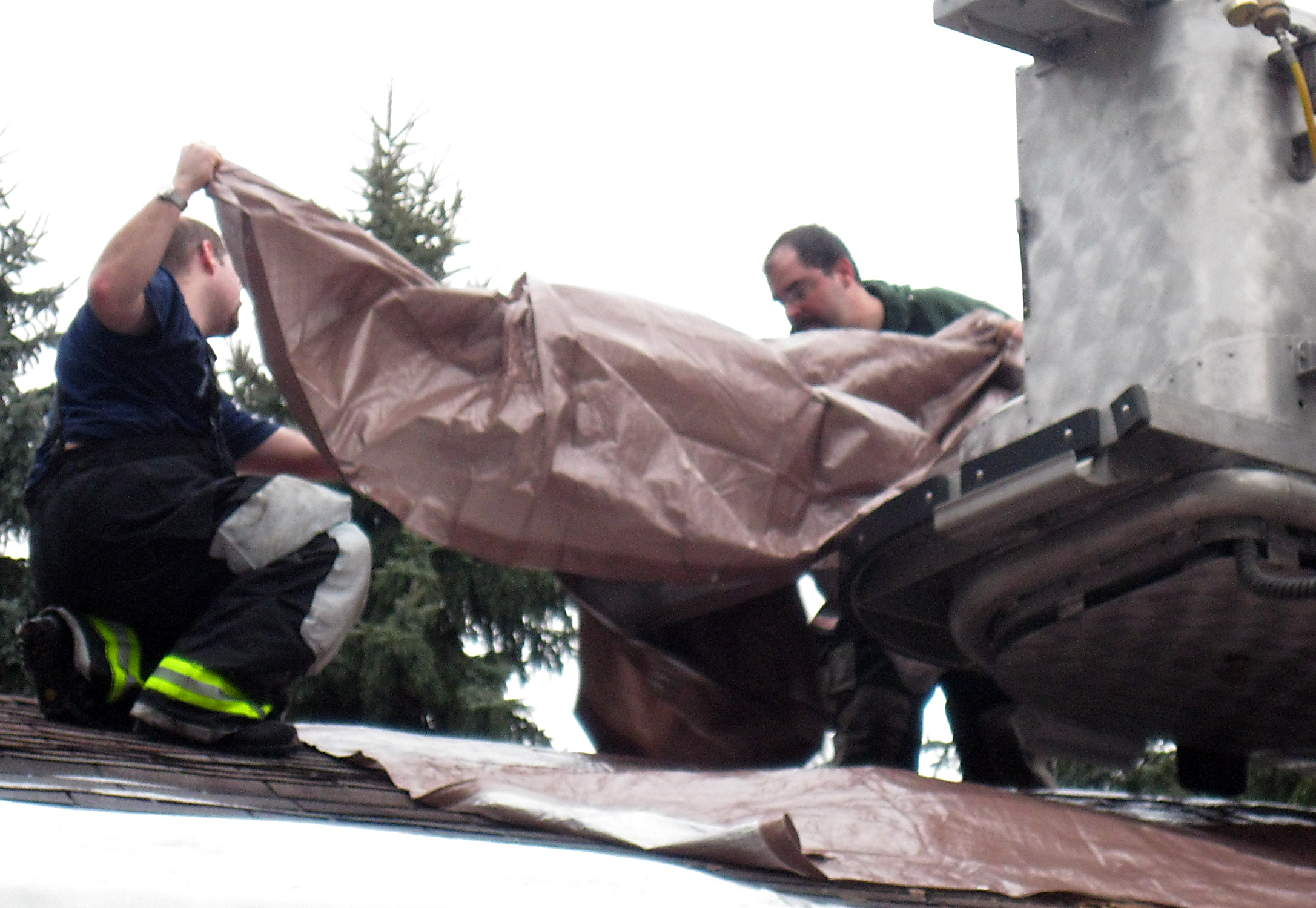 Ron Stiles and Assistant Chief Dan Shepler lay down tarps over the roof's hole. (Steven McDole)