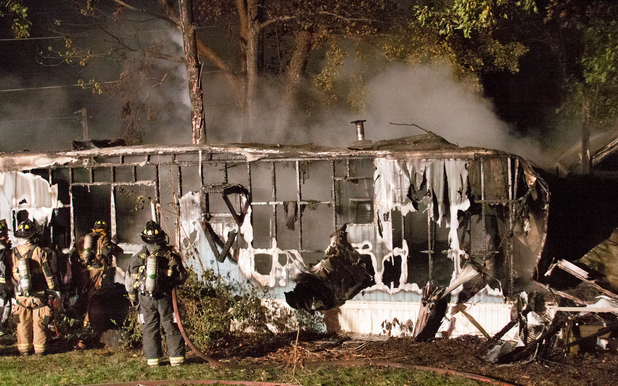 Firefighters stand outside the shell of the former trailer.