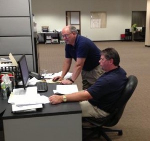 Dennis Parr, manager of Engineering Services at Global Fabrication (standing) reviews data on company production costs with intern DavidWachob. (Provided photo) 