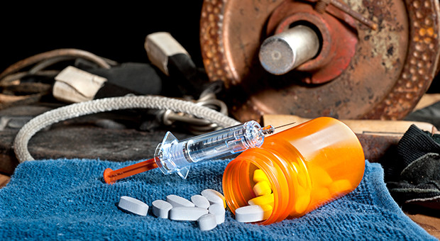 Steroid medication including pills and a syringe in front of exercise equipment.  Image can be used for steroid and performancing enhancement inferences in sports.