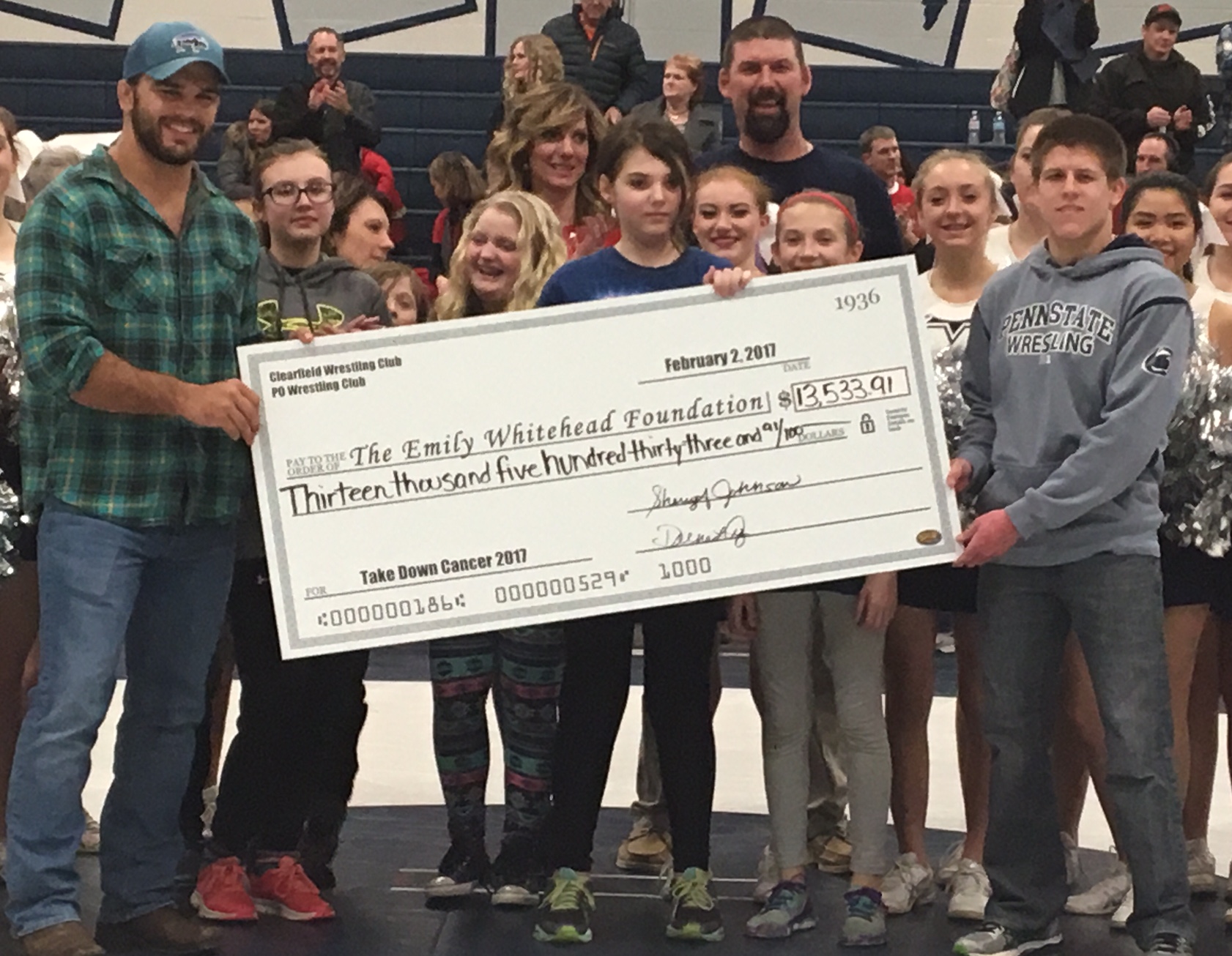 With her mom over her right shoulder and dad over her left, Emily Whitehead holds the ceremonial check that will go to her foundation. Check presenters were former PSU wrestlers Morgam McIntosh and Jordan Conaway