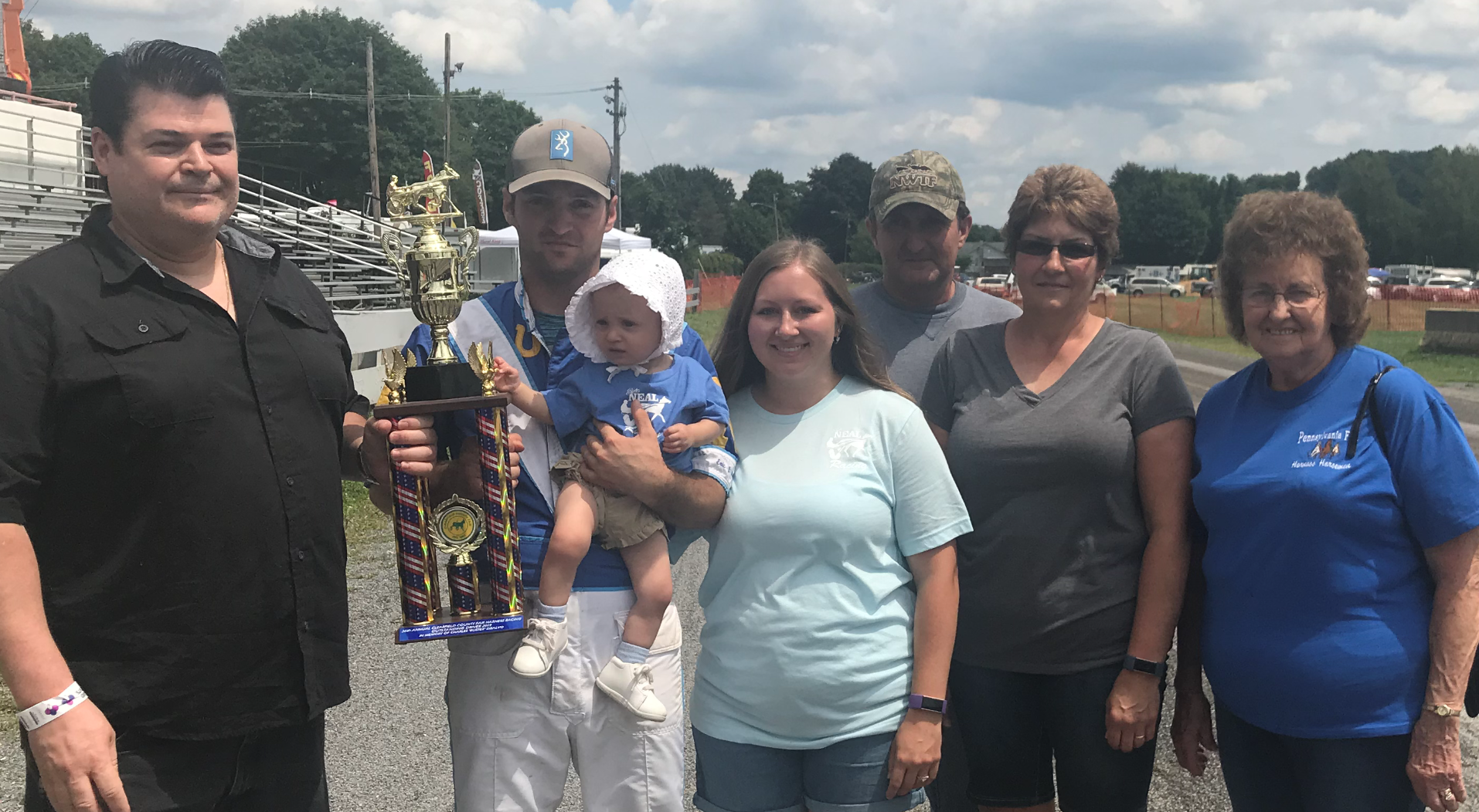 FIRST-TIME WINNER Eric Neal of Punxsutawney accepts the Charles "Buster" DiSalvo Trophy for the most wins in the Clearfield County Fair harness racing meet from John Spingola while holding 10-month-old daughter Hazel. Neal is flanked by Holly Waltman, his fiancé, father Randy Neal, mother Suzie Neal and grandmother Donna Neal. (Photo by Sue Kavelak)
