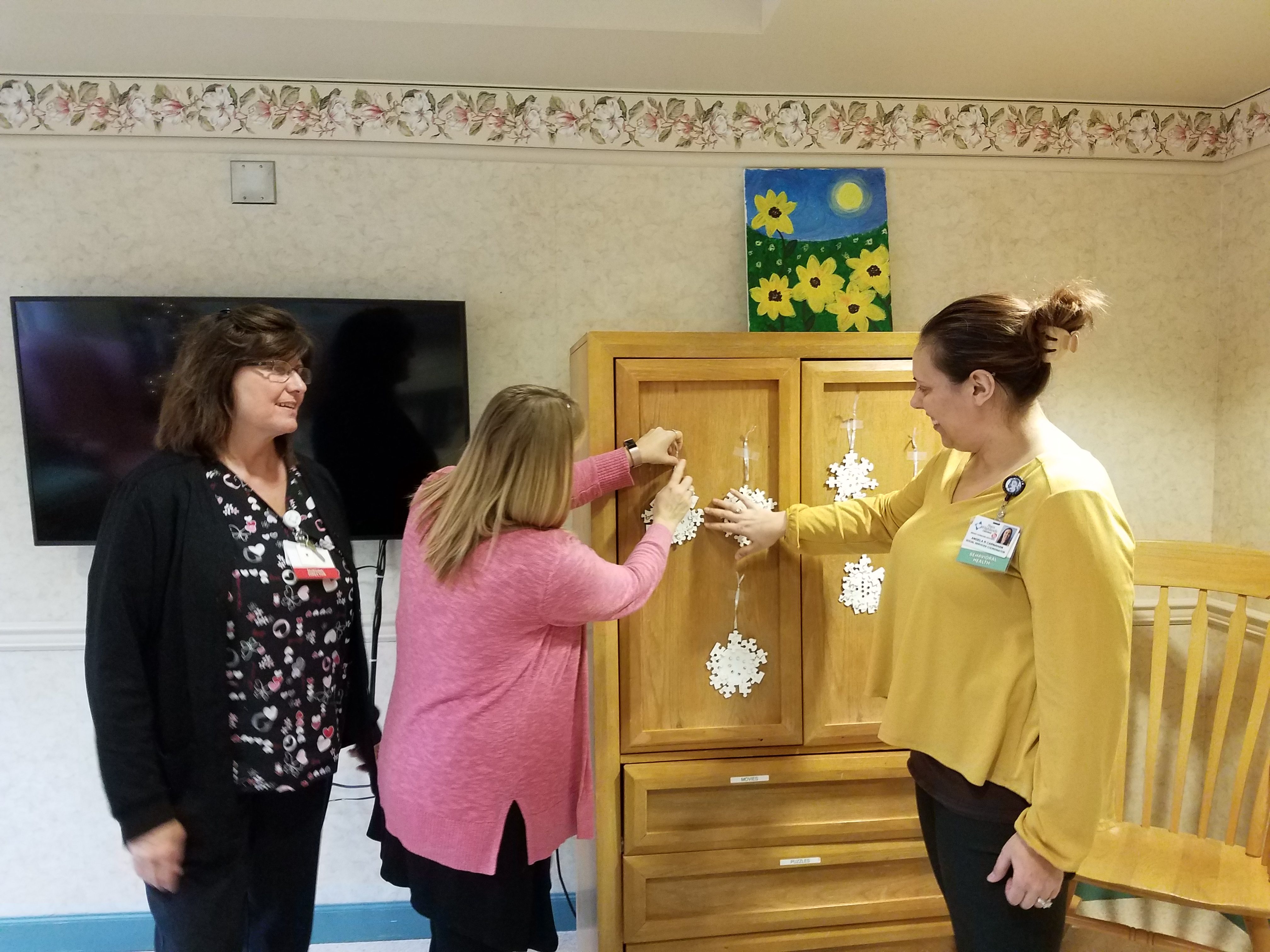 Sharon Goodman, Behavioral Health Inpatient Director, left, hangs snowflakes with staff members at Bright Horizons Inpatient Clinic at Penn Highlands Clearfield. The snowflakes were made as an arts and crafts project by patients of the clinic. The short-term inpatient facility provides a multitude of behavioral health services to patients 55 and older (Photo by Kimberly Finnigan)