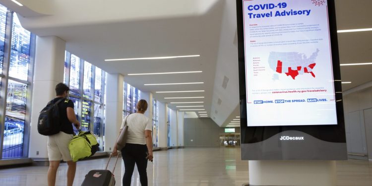 Arriving travelers walk by a sign in the baggage claim area of Terminal B at LaGuardia Airport, Thursday, June 25, 2020, in New York. New York, Connecticut and New Jersey are asking visitors from states with high coronavirus infection rates to quarantine for 14 days. The “travel advisory” affects three adjacent Northeastern states that managed to check the spread of the virus this spring as New York City became a hot spot. Travelers from mostly southern and southwestern states including Florida, Texas Arizona and Utah will be affected starting Thursday. The two-week quarantine will last two weeks from the time of last contact within the identified state. (AP Photo/Kathy Willens)