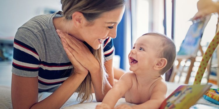 Mother is playing with her little baby on the bed