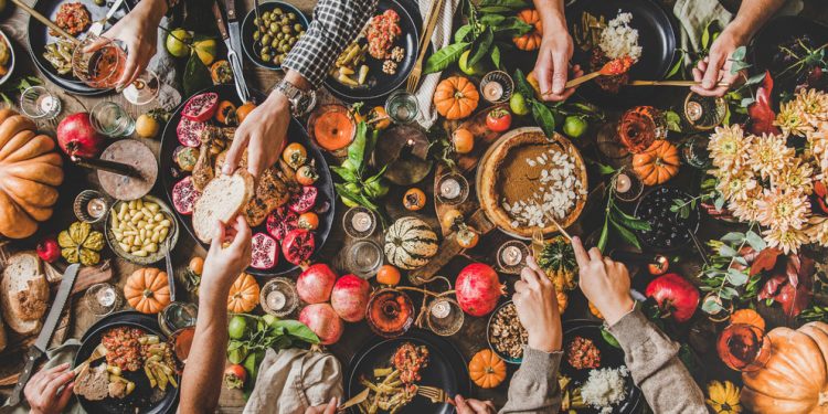 Family celebrating Thanksgiving day. Flat-lay of eating and drinking peoples hands over Friendsgiving table with traditional Fall food, roasted turkey, candles, pumpkin pie, top view