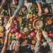 Family celebrating Thanksgiving day. Flat-lay of eating and drinking peoples hands over Friendsgiving table with traditional Fall food, roasted turkey, candles, pumpkin pie, top view