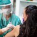 Female doctor in protective workwear disinfecting female patient's skin for vaccination; prevention and immunization from corona virus infection