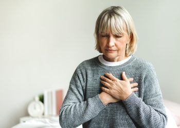 Senior adult elderly women sit on bed with chest pain suffering from heart attack in the bedroom.Healthcare and medical concept