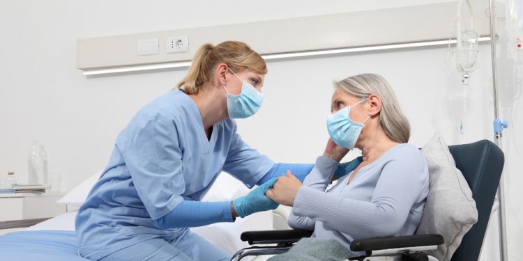 nurse take comfort elderly woman in wheelchair wearing surgical protective medical masks in hospital room, concept of isolation from corona virus covid 19