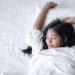 Beautiful young pretty Asian woman wake up and make happy smile with white shirt at the white bed in the morning.