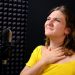 A young woman holding her throat near the microphone, black background. The voice of the singer when recording a song in the music Studio. Voice failure, hoarseness, pain in the vocal cords.