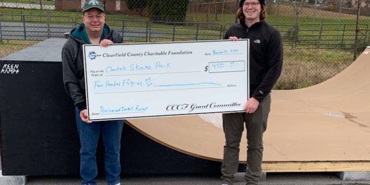 Mark McCracken, executive director of the Clearfield County Charitable Foundation presents Dalton Kendrick from the Clearfield Skate Park Committee a CCCF grant to help fund the ramp purchase and installation.   The new ramp is pictured in the background. (Provided photo)