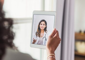 A female doctor offers an unrecognizable female patient advice during a telemedicine appointment.