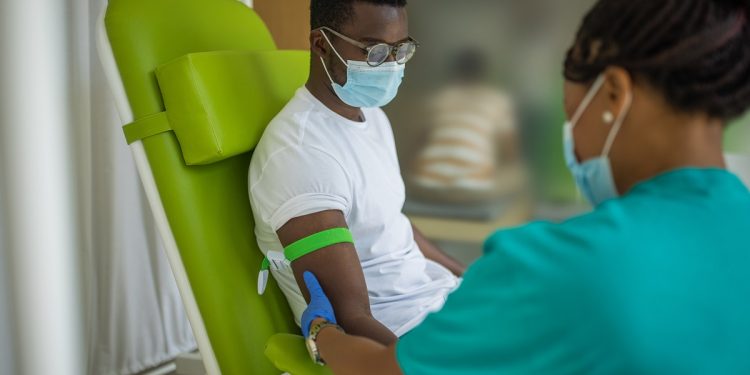 Young man on blood donation at medical clinic, nurse and him are wearing protective face masks for protection against coronavirus