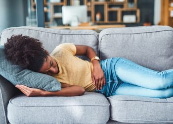 Shot of a young woman experiencing stomach pain while lying on the sofa at home