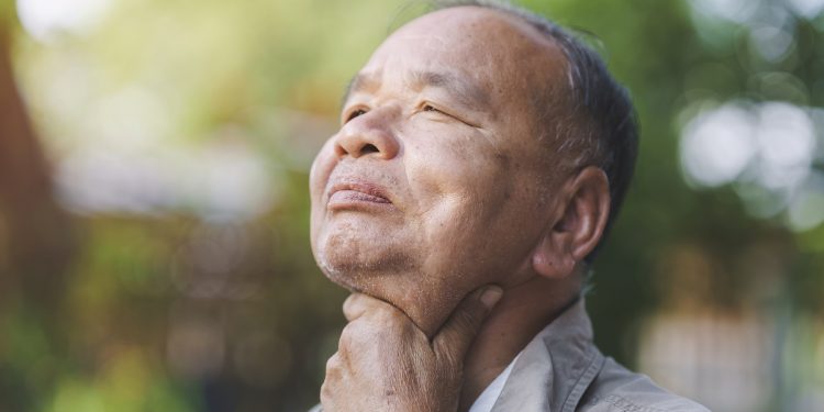 An elderly man has a sore throat due to flu or COVID-19. Concept of sickness of the elderly.