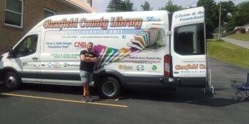 The Clearfield County Public Library’s new Mobile Services Outreach Coordinator, Chase Skrzypek, poses outside the Mobile Service Unit. Chase took over the position in April and is enjoying learning about the patrons scattered throughout the county. (Photo by Julie Rae Rickard)