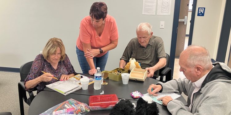 Adult Day Center Director Julie Fenton, standing, talks with consumers about the various activities they are engaged in at the center. They are, left to right, Doris, Jim and Larry.