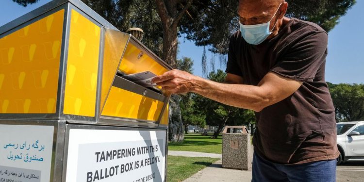 A man wearing a face mask drops his ballot into an official ballot drop box during the 2020 elections.

Shutterstock