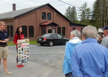 Brian Leech (left) led the walk in Falls Creek. The tour is outside the former Gray Printing Company Building. Sarah Zwick holds a display board of historic photos of Falls Creek. (Provided photo)