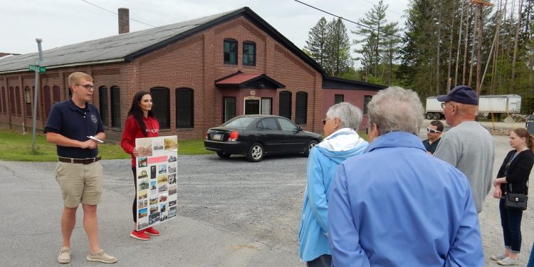 Brian Leech (left) led the walk in Falls Creek. The tour is outside the former Gray Printing Company Building. Sarah Zwick holds a display board of historic photos of Falls Creek. (Provided photo)