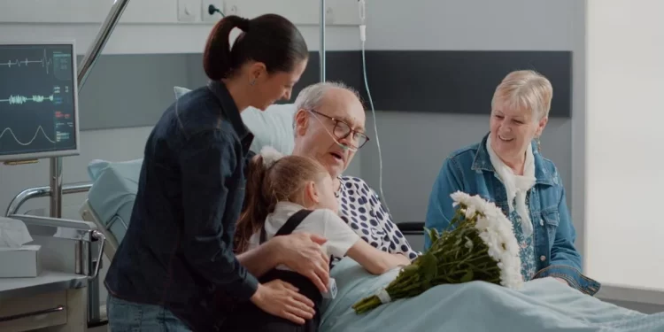 Family visiting elder patient with illness in hospital ward bed. Mother and child bringing flowers to grandpa at visit in intensive care room. Visitors giving comfort to old man. Handheld shot

DC Studio | Shutterstock