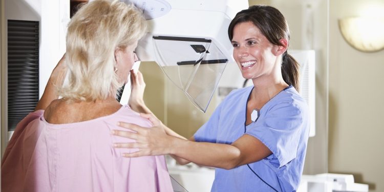 Woman, 50s, with nurse or technician, getting a mammogram.  Focus on nurse.