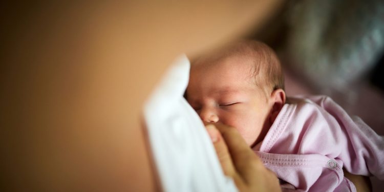 Close up of newborn baby girl being breastfed during her sleep.