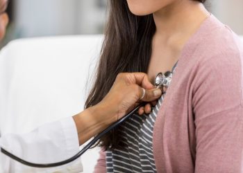 Unrecognizable doctor listens to a teenage patient's heartbeat