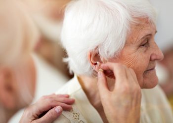 Female doctor applying hearing aid to senior woman's ear