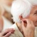 Female doctor applying hearing aid to senior woman's ear