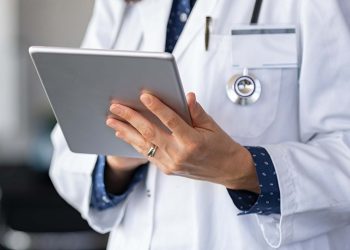 Close up of woman doctor hands using digital tablet at clinic. Closeup of female doctor in labcoat and stethoscope holding digital tablet, reading patient report. Hands holding medical report, copy space.