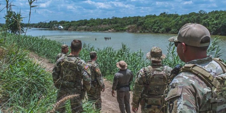 Soldiers from the Texas National Guard watch a Border Patrol helicopter hover above a group of civilians wading in the Rio Grande River along the Texas-Mexico border, May 22, 2023. The Soldiers patrol the southern border in support of Operation Lone Star to detect, deter, and interdict illegal immigrants before they enter Texas communities.

Pvt. Steven Day | Texas National Guard