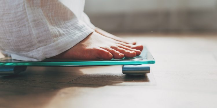 Female feet standing on electronic scales for weight control on wooden background. The concept of slimming and weight loss