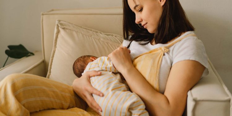 Newborn baby boy sucking milk from mothers breast. Portrait of mom and breastfeeding baby. Concept of healthy and natural baby breastfeeding nutrition.