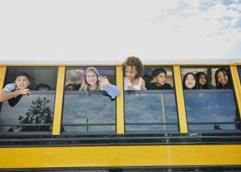 Medium wide shot of smiling middle school kids looking out open windows of school bus