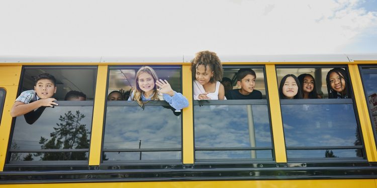 Medium wide shot of smiling middle school kids looking out open windows of school bus