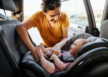 Mother putting baby girl in baby car seat