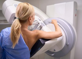 Back view of Caucasian female patient undergoing 3D mammography in radiology room