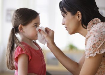 Mother wiping nose of daughter with tissue