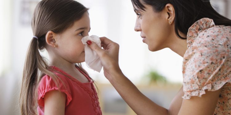 Mother wiping nose of daughter with tissue