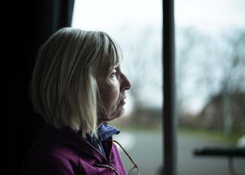 Lonely senior woman looking out of her window.