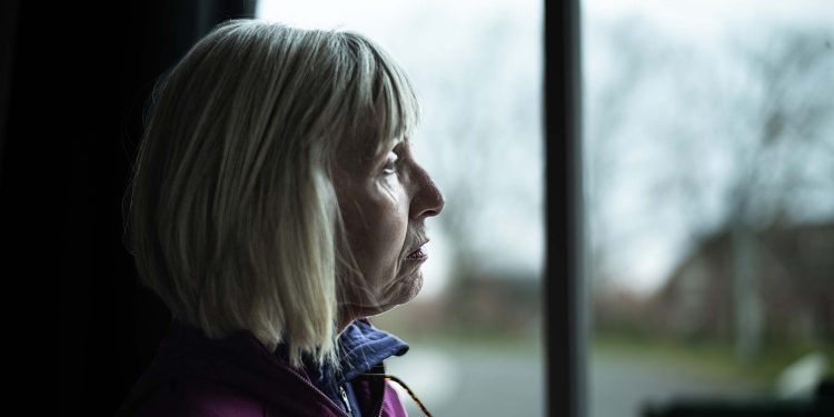 Lonely senior woman looking out of her window.